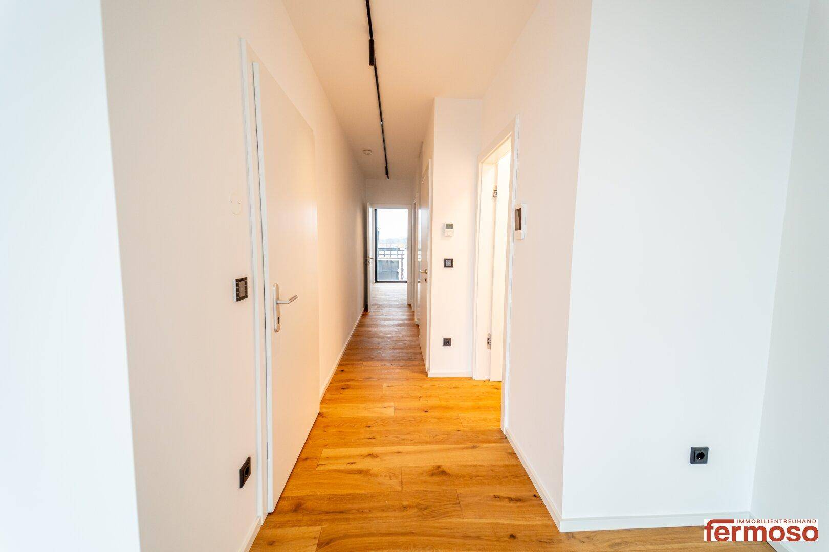 Langer, heller Flur mit Holzboden und modernen Deckenleuchten, der die Räume verbindet.