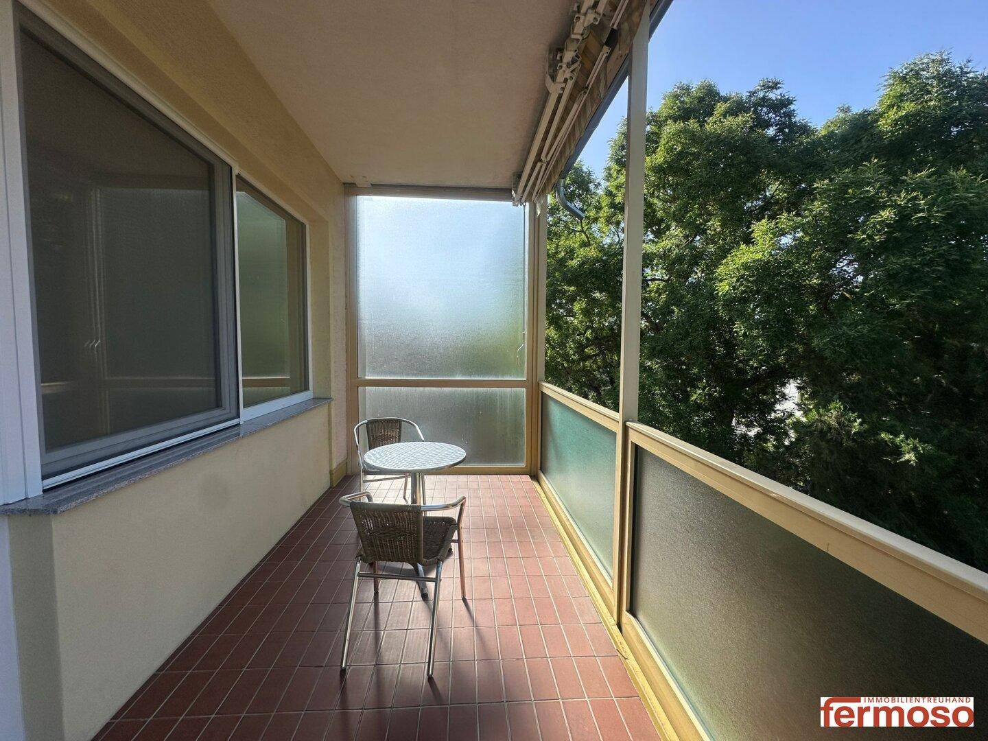 Gemütlicher, verglaster Balkon mit Sitzgelegenheiten und Blick auf die grüne Umgebung.