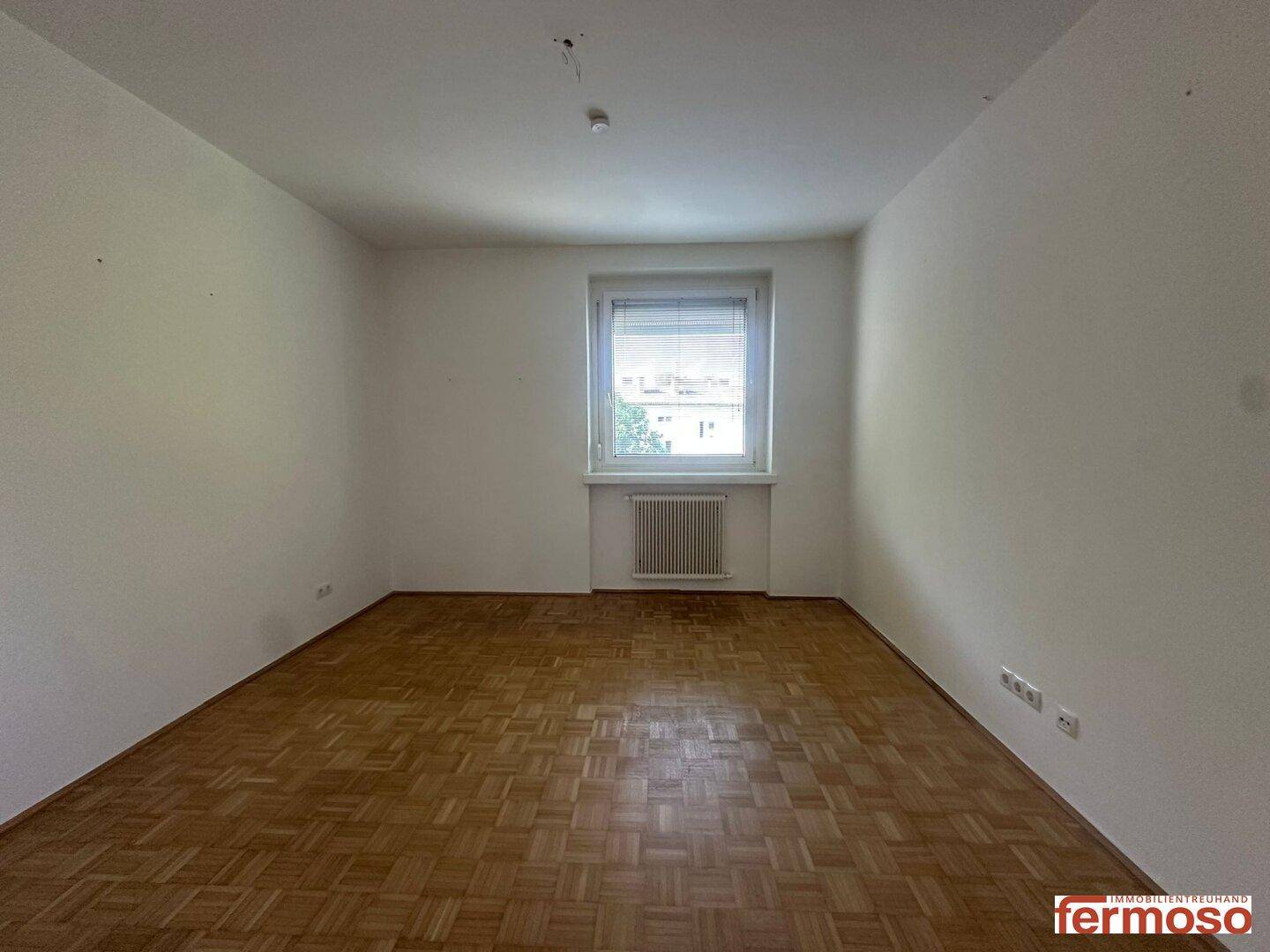 Helles Zimmer mit Parkettboden und Fenster, das sich gut als Schlaf- oder Arbeitszimmer eignet.