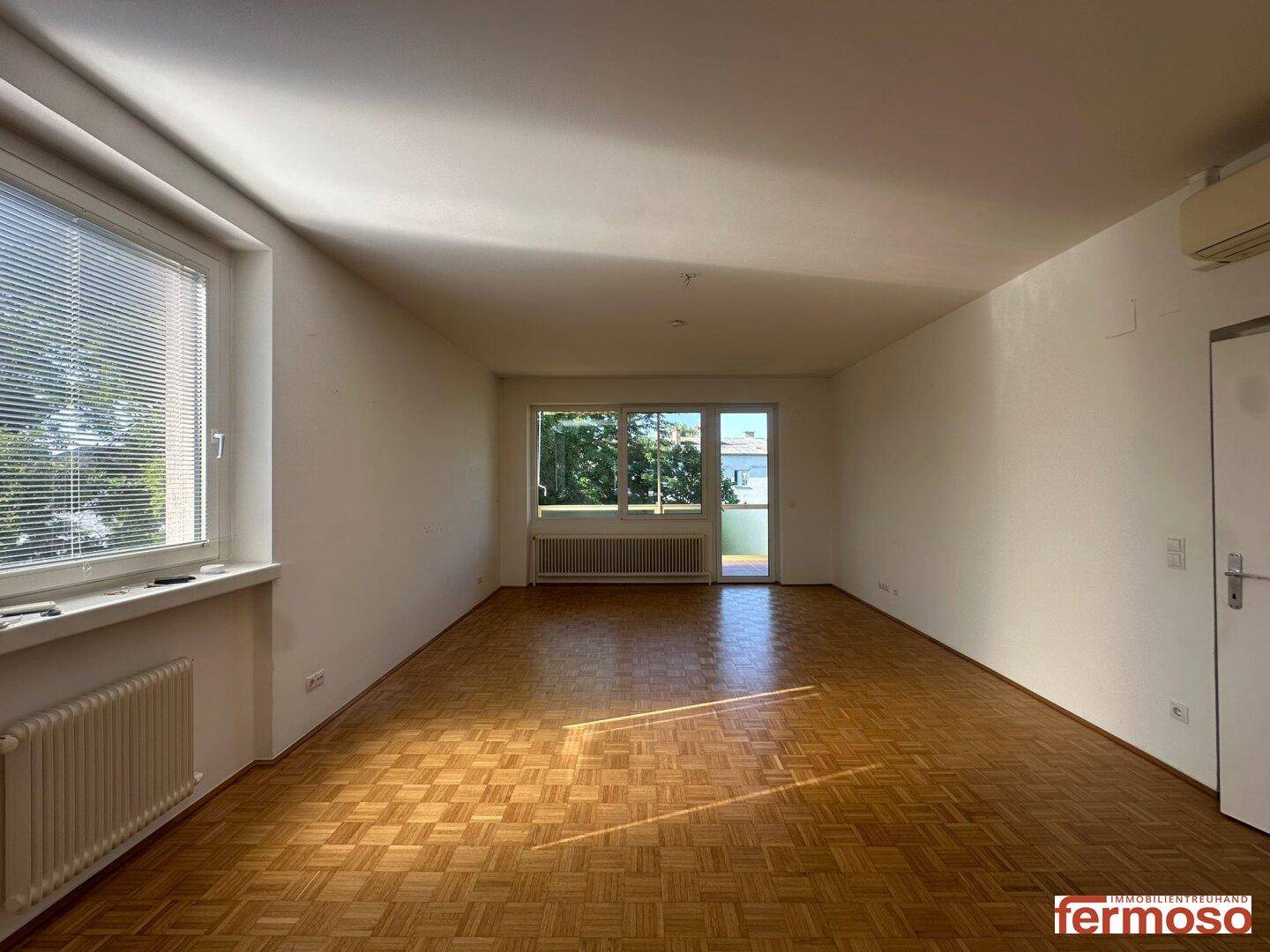 Großes, lichtdurchflutetes Wohnzimmer mit Parkettboden und Zugang zu einem Balkon.