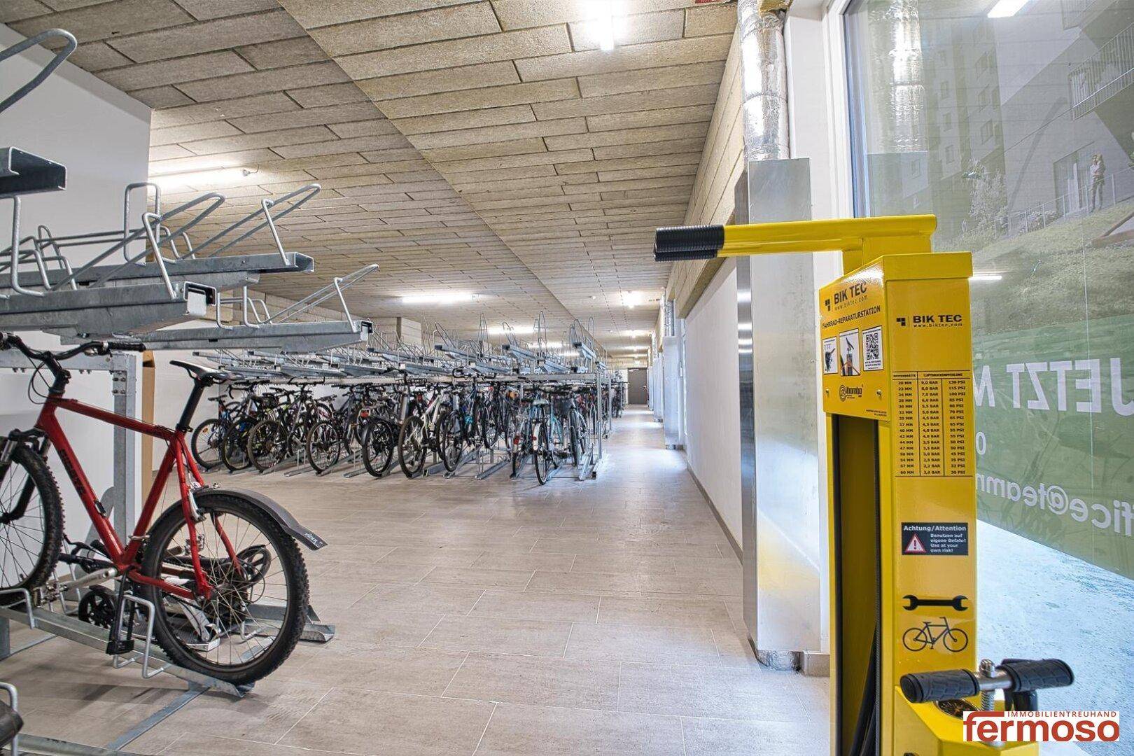 Großer Fahrradraum mit zahlreichen Stellplätzen und einer praktischen Reparaturstation für Fahrräder.