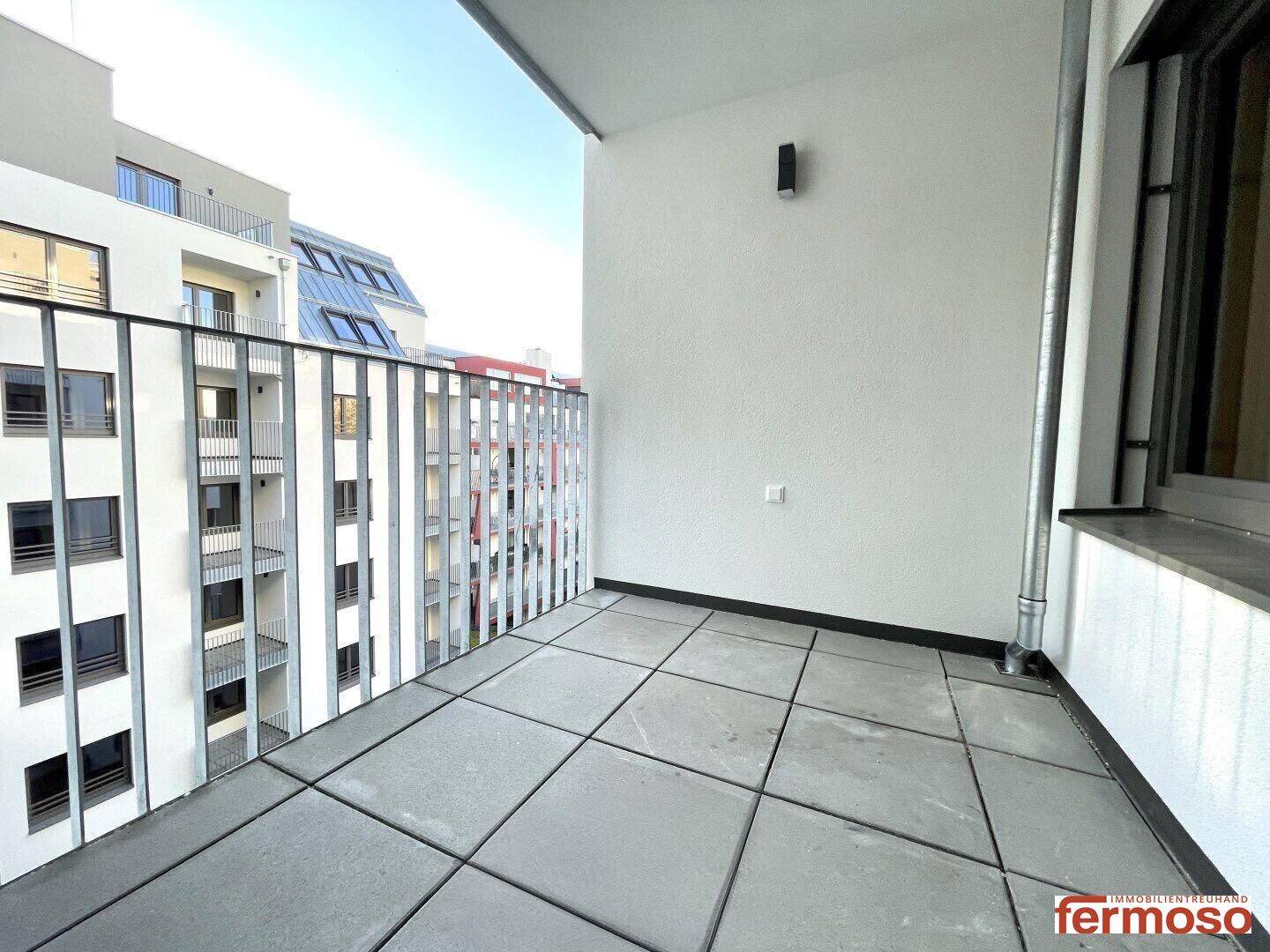 Geräumiger Balkon mit Fliesenboden und modernem Metallgeländer, mit Blick auf die umliegenden Gebäude.