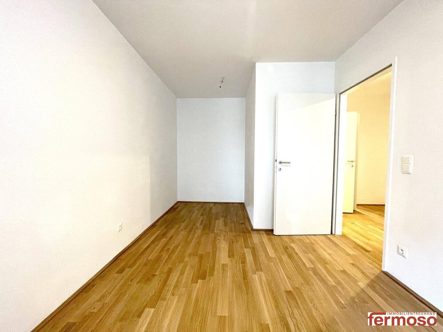 Leeres Zimmer mit hellem Holzboden und weißer Tür, bereit zur individuellen Gestaltung und Einrichtung.