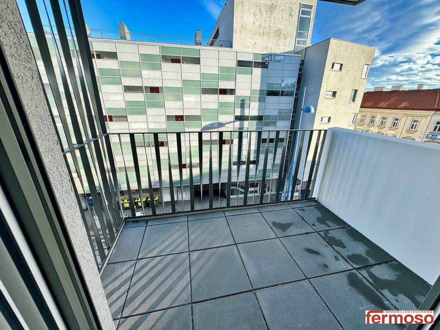 Kleiner Balkon mit Fliesenboden und Blick auf die umliegenden Gebäude.