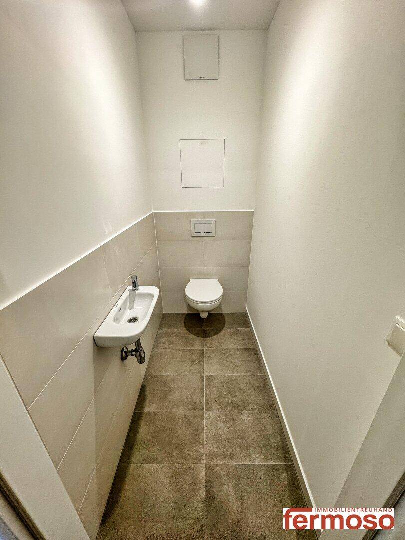 Separates Gäste-WC mit Wand-WC und kleinem Handwaschbecken, modern gefliest.