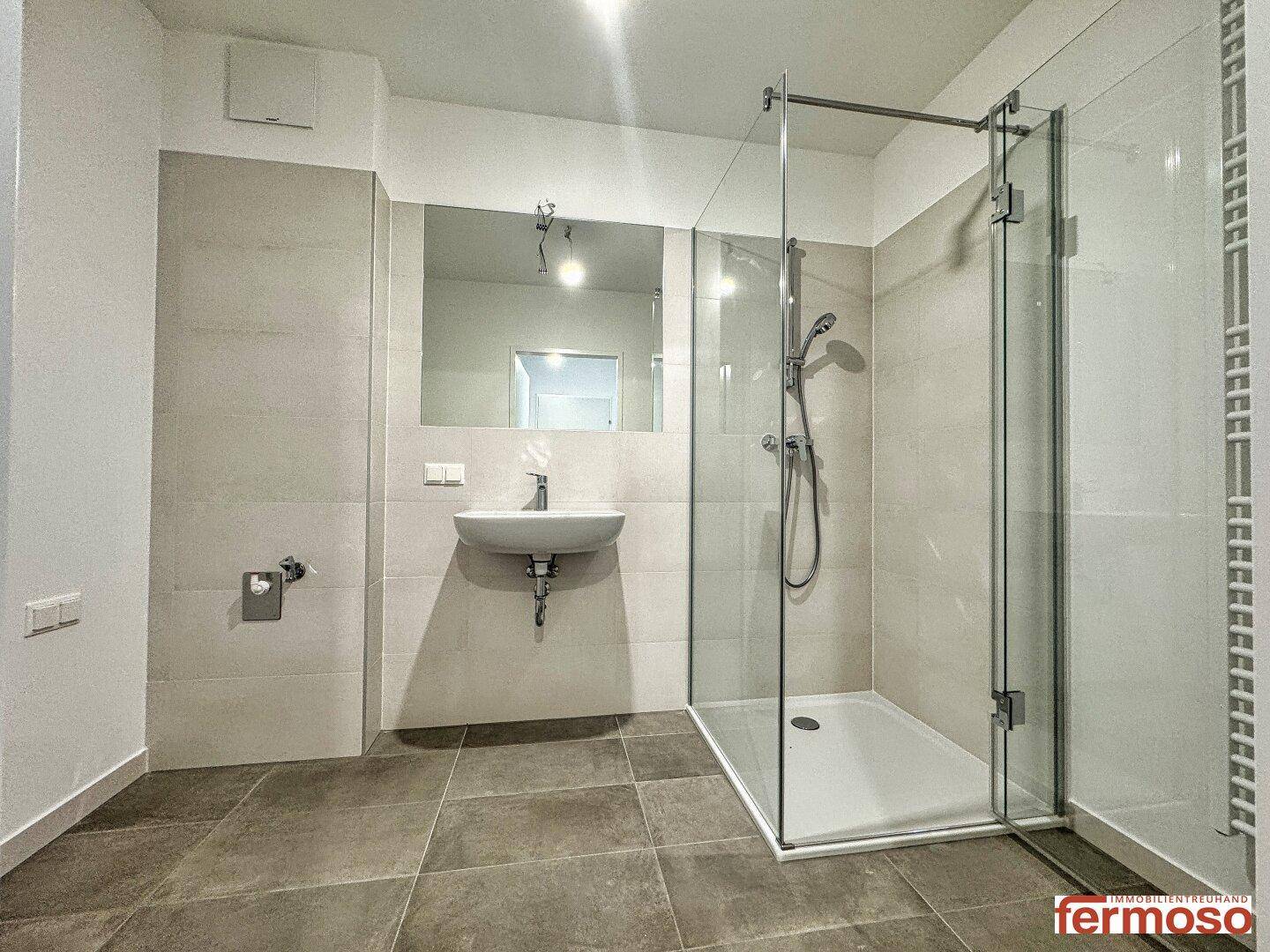 Zeitgemäßes Badezimmer mit großer Duschkabine, Wandspiegel und grauen Fliesen.