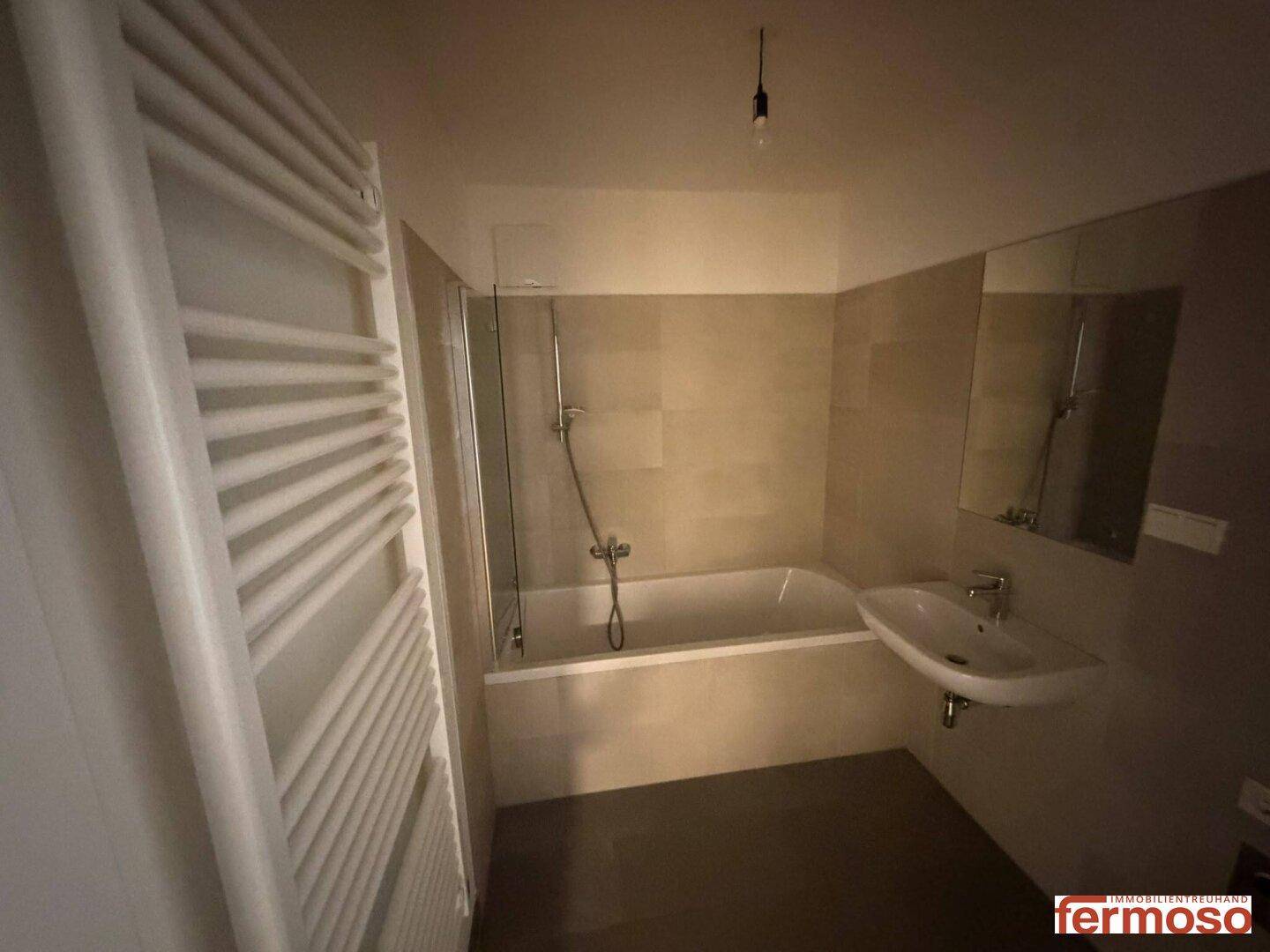 Modernes Badezimmer mit Badewanne, Duschfunktion, Waschbecken und beheiztem Handtuchhalter.