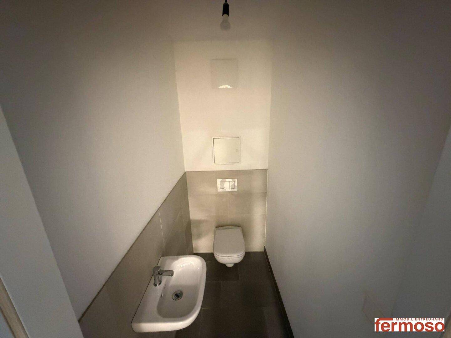 Separates Gäste-WC mit wandhängender Toilette und kleinem Handwaschbecken.