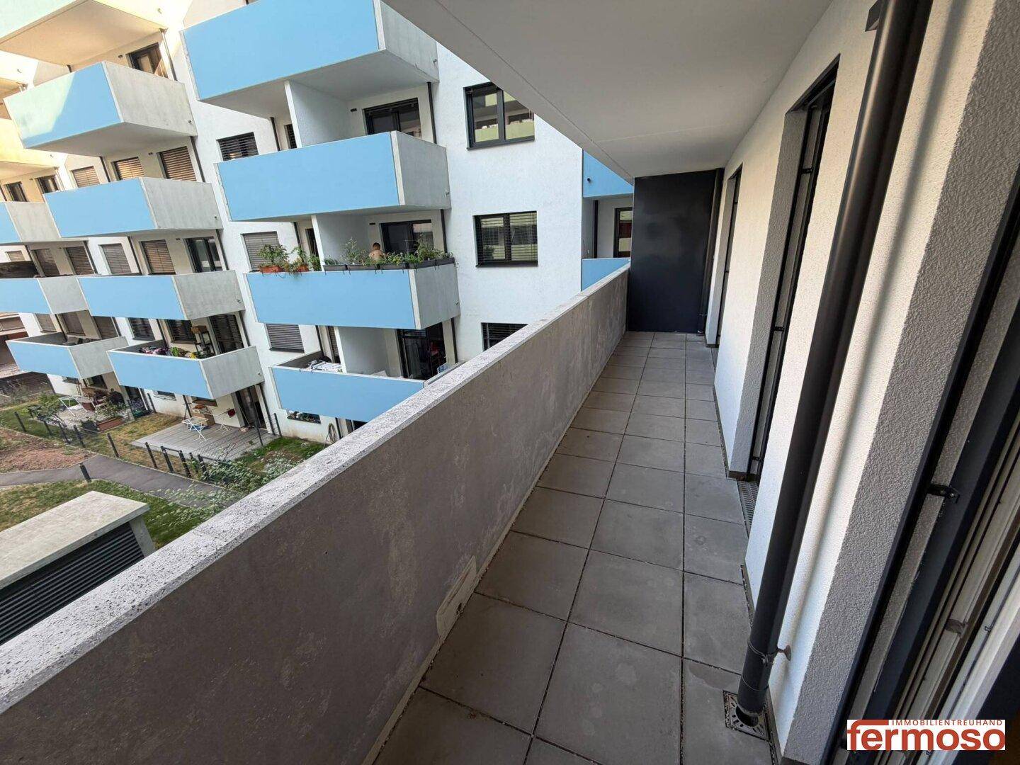 Langer Balkon mit Fliesenboden und Blick auf die umliegenden Gebäude der Wohnanlage.