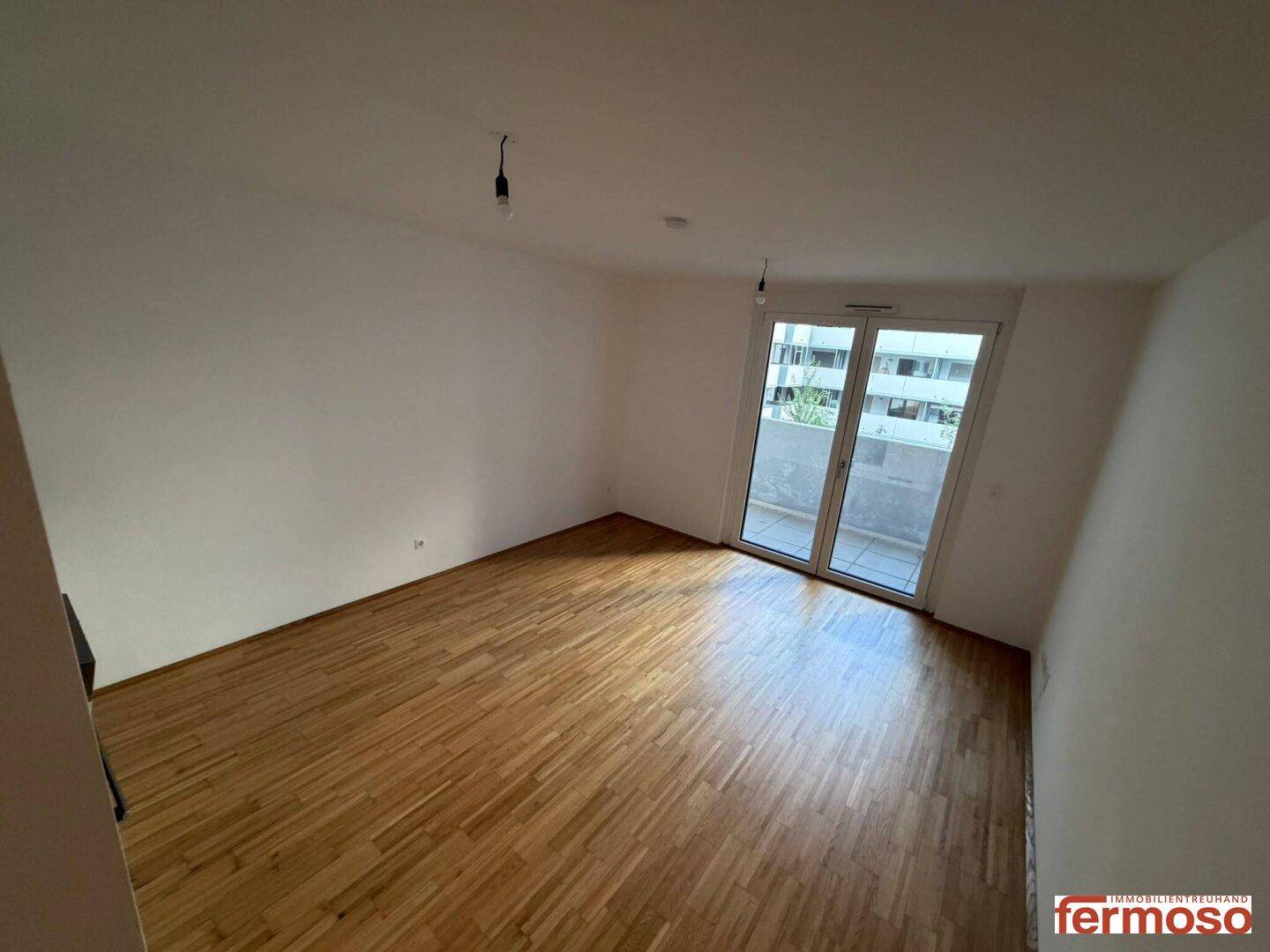 Geräumiges Zimmer mit Parkettboden und großen Fenstern, die Zugang zum Außenbereich bieten.