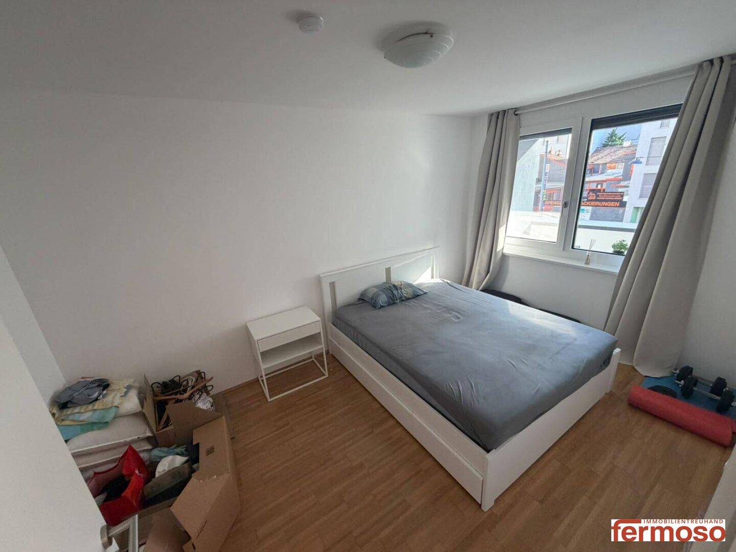 Helles Schlafzimmer mit Holzbett, Nachttisch und großem Fenster für viel Tageslicht.
