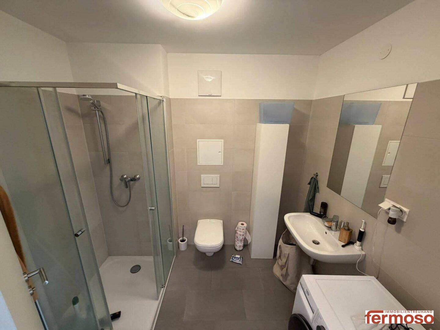 Modernes Badezimmer mit Duschkabine, WC, Waschbecken und Waschmaschine.