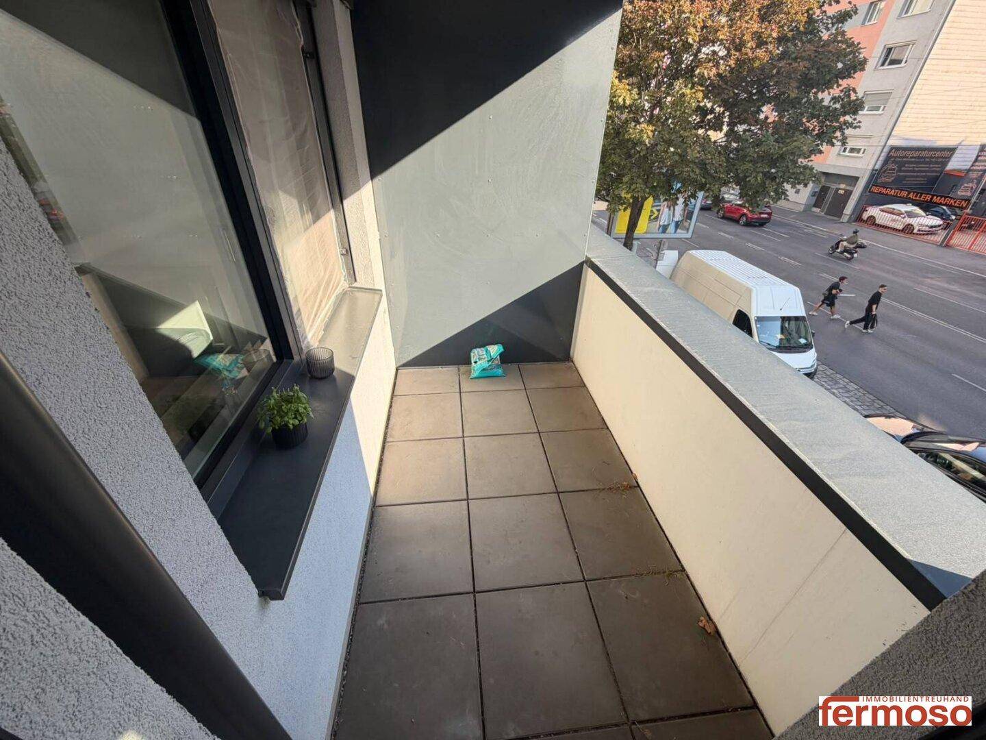 Kleiner Balkon mit Fliesenboden und Blick auf die belebte Straße.