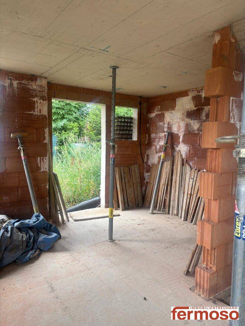 Rohbau eines Raumes mit Ziegelwänden, Baustützen und einer Fensteröffnung mit Blick nach draußen.