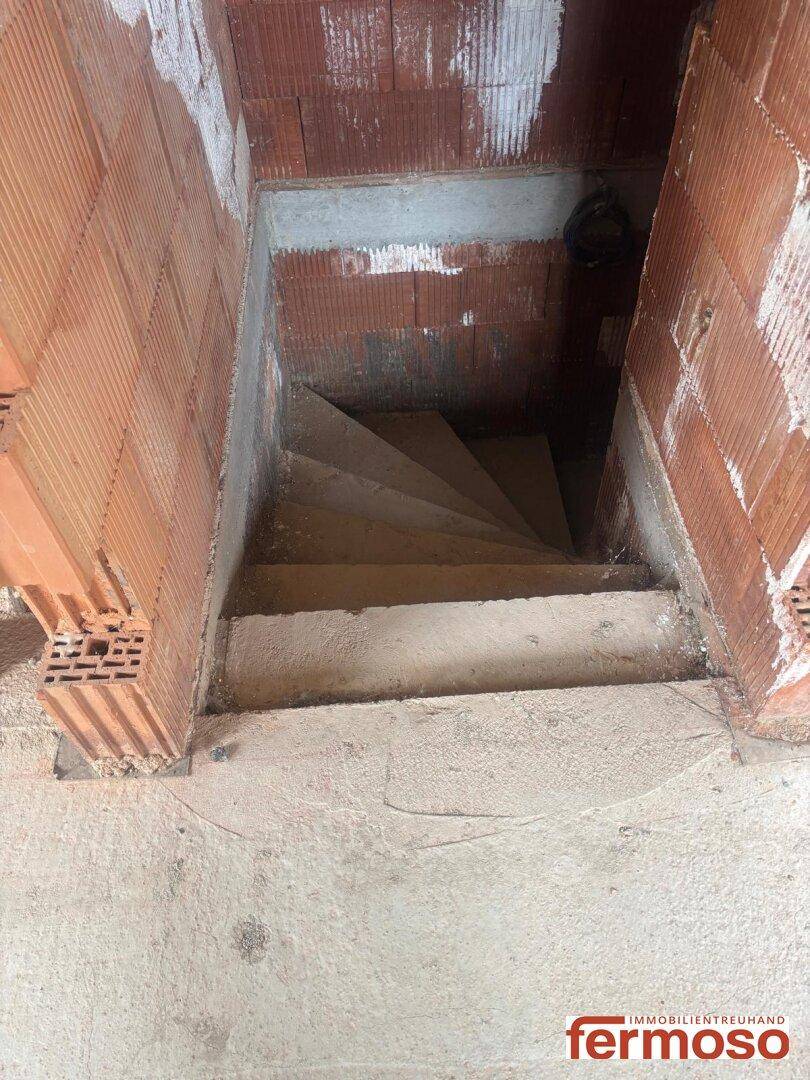 Betontreppe im Rohbau eines Gebäudes, umgeben von Ziegelwänden, die in ein Untergeschoss führt.