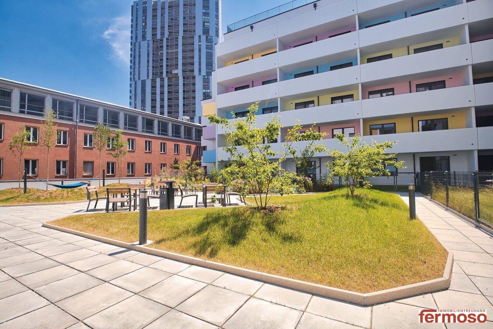 Gepflegter Gemeinschaftsgarten mit Sitzgelegenheiten und Grünflächen zwischen modernen Gebäuden.