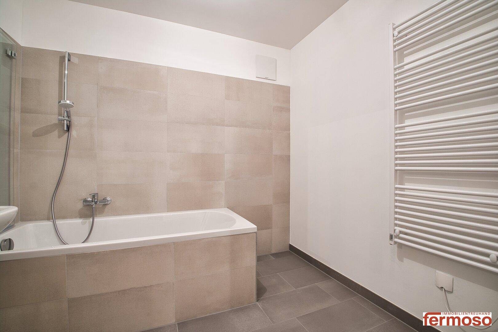 Modernes Badezimmer mit Badewanne, Duschfunktion und beheiztem Handtuchhalter.