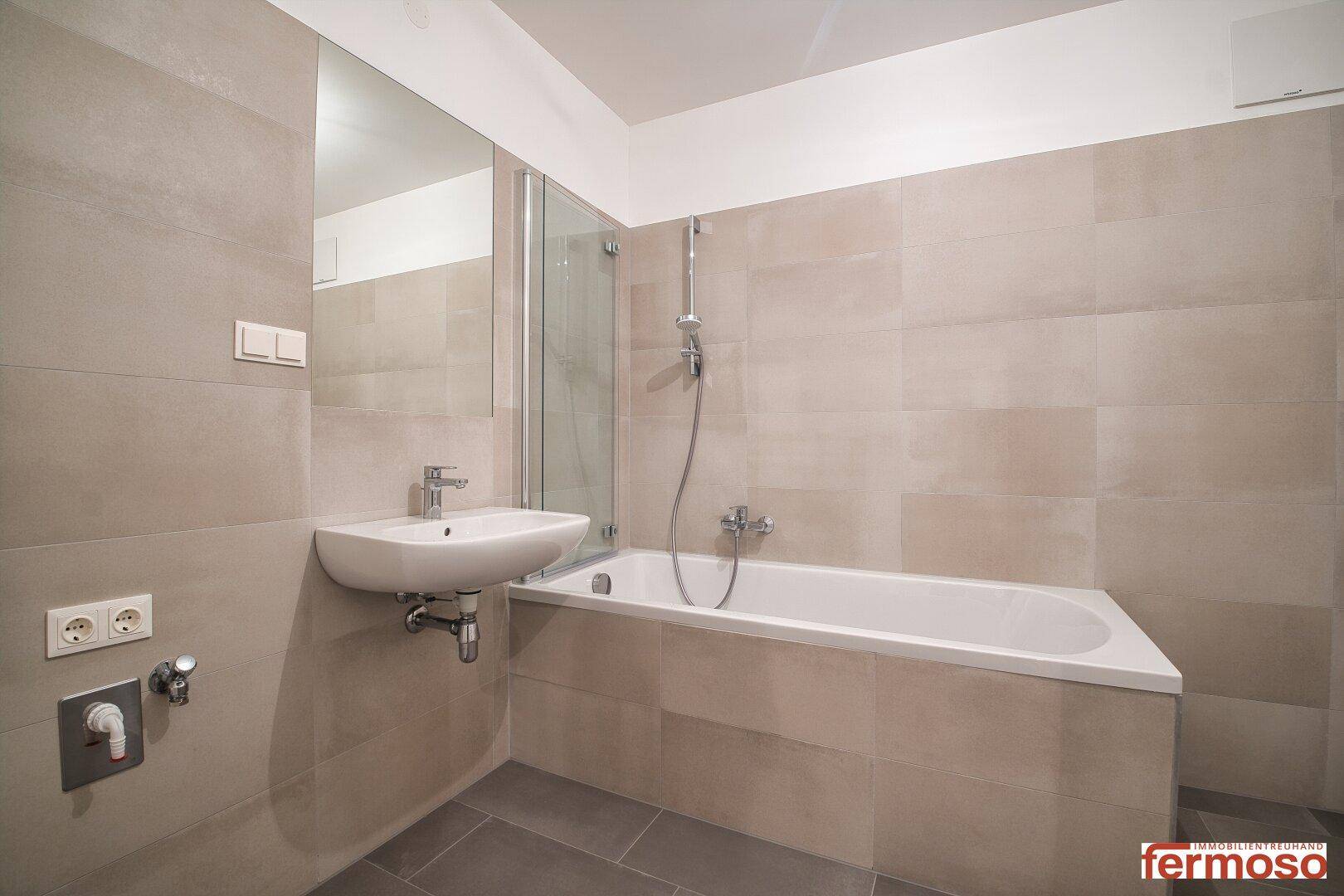 Helles Badezimmer mit Badewanne, Duschabtrennung und modernem Waschbecken.