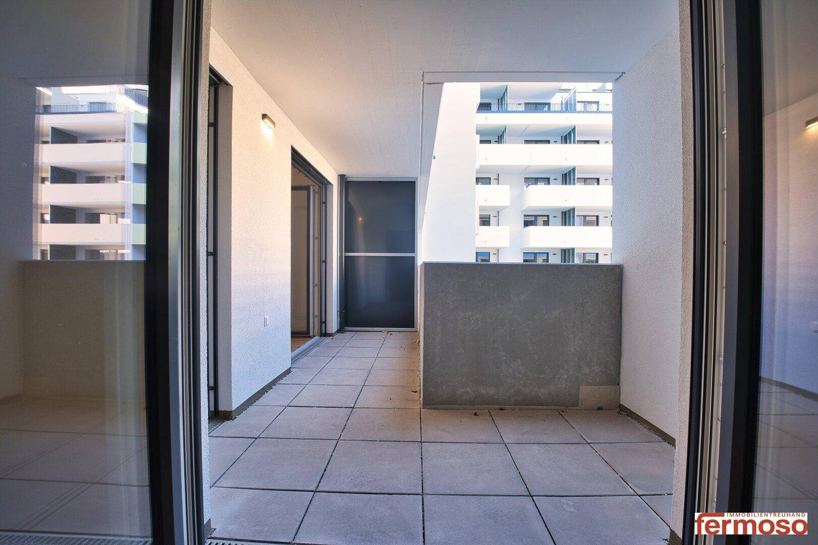 Heller Balkon mit Fliesenboden und Blick auf die umliegenden Wohngebäude.
