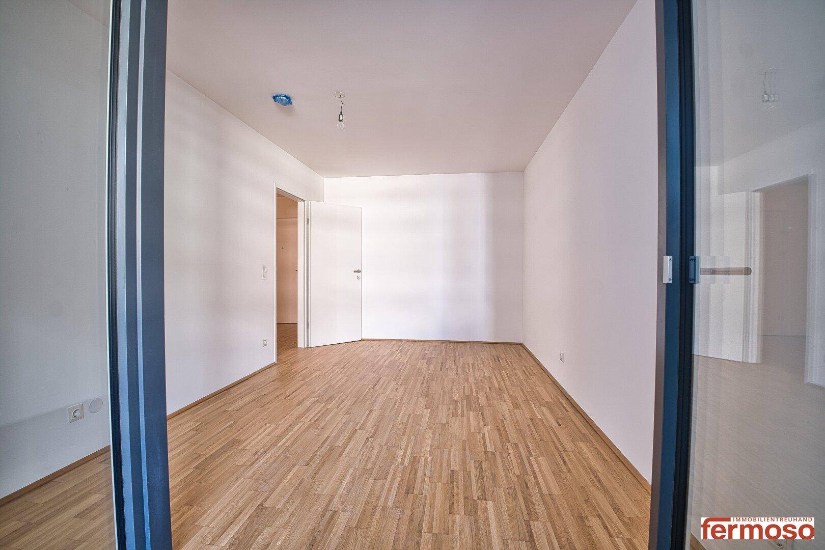 Geräumiges, helles Zimmer mit Parkettboden, vom Balkon aus gesehen, bereit zur Einrichtung.