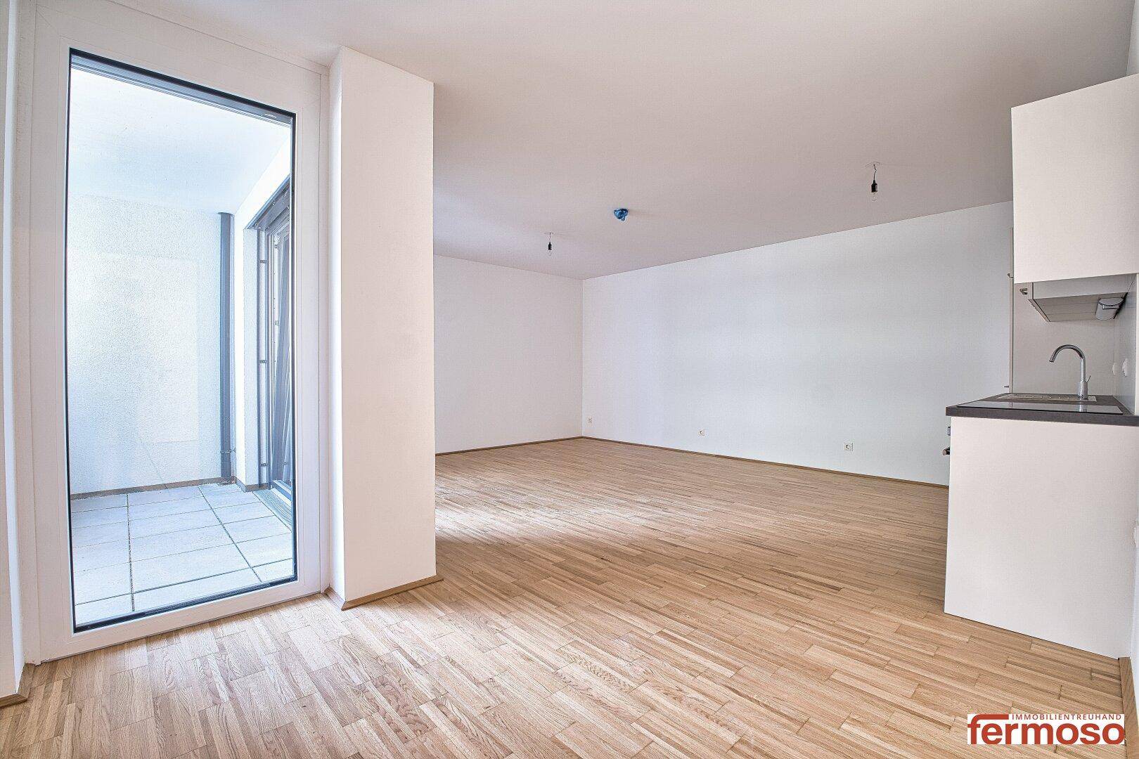 Heller Wohnbereich mit Parkettboden und großem Fenster, das Zugang zum Balkon bietet.