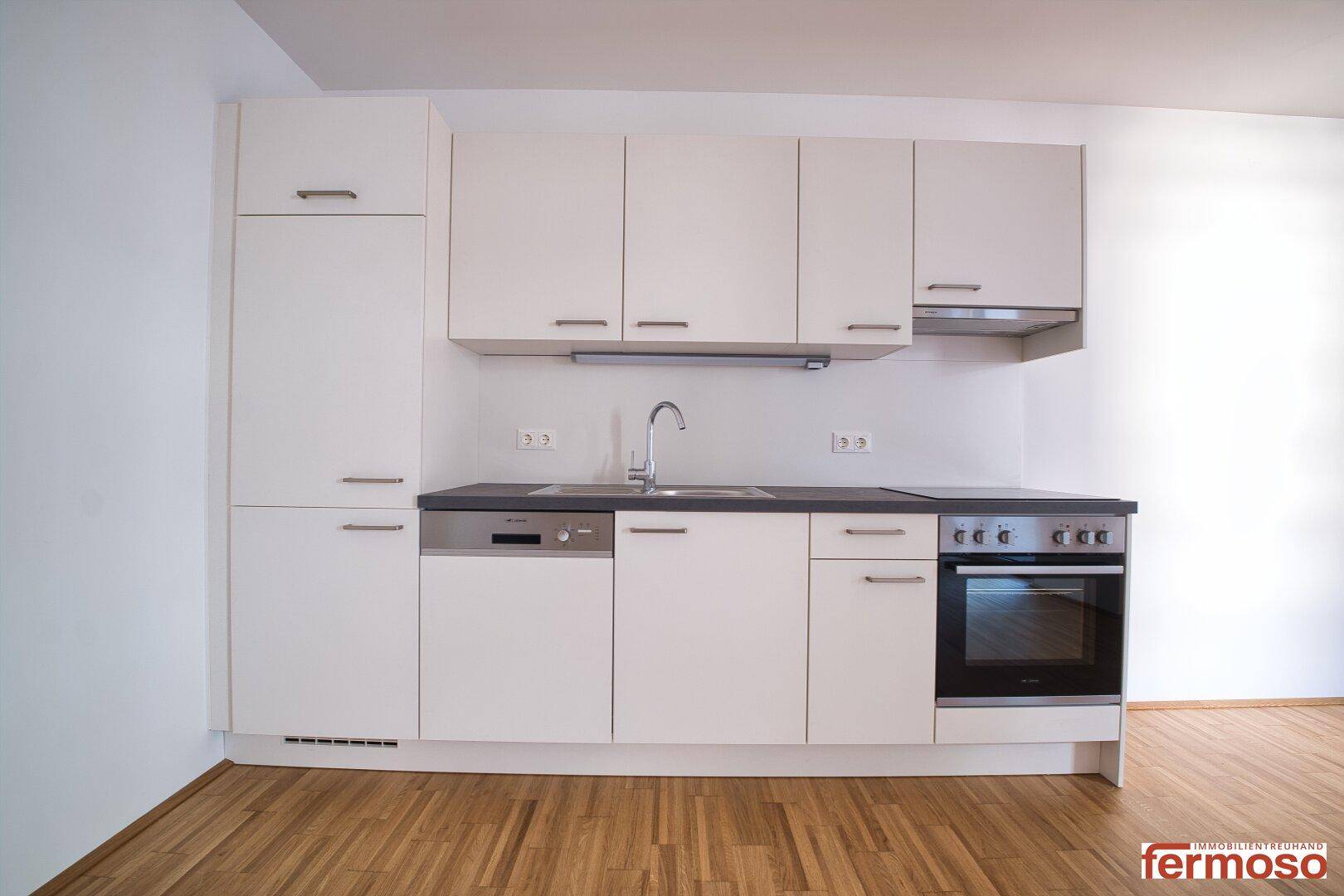 Moderne Einbauküche mit weißen Schränken, dunkler Arbeitsplatte und integrierten Geräten.