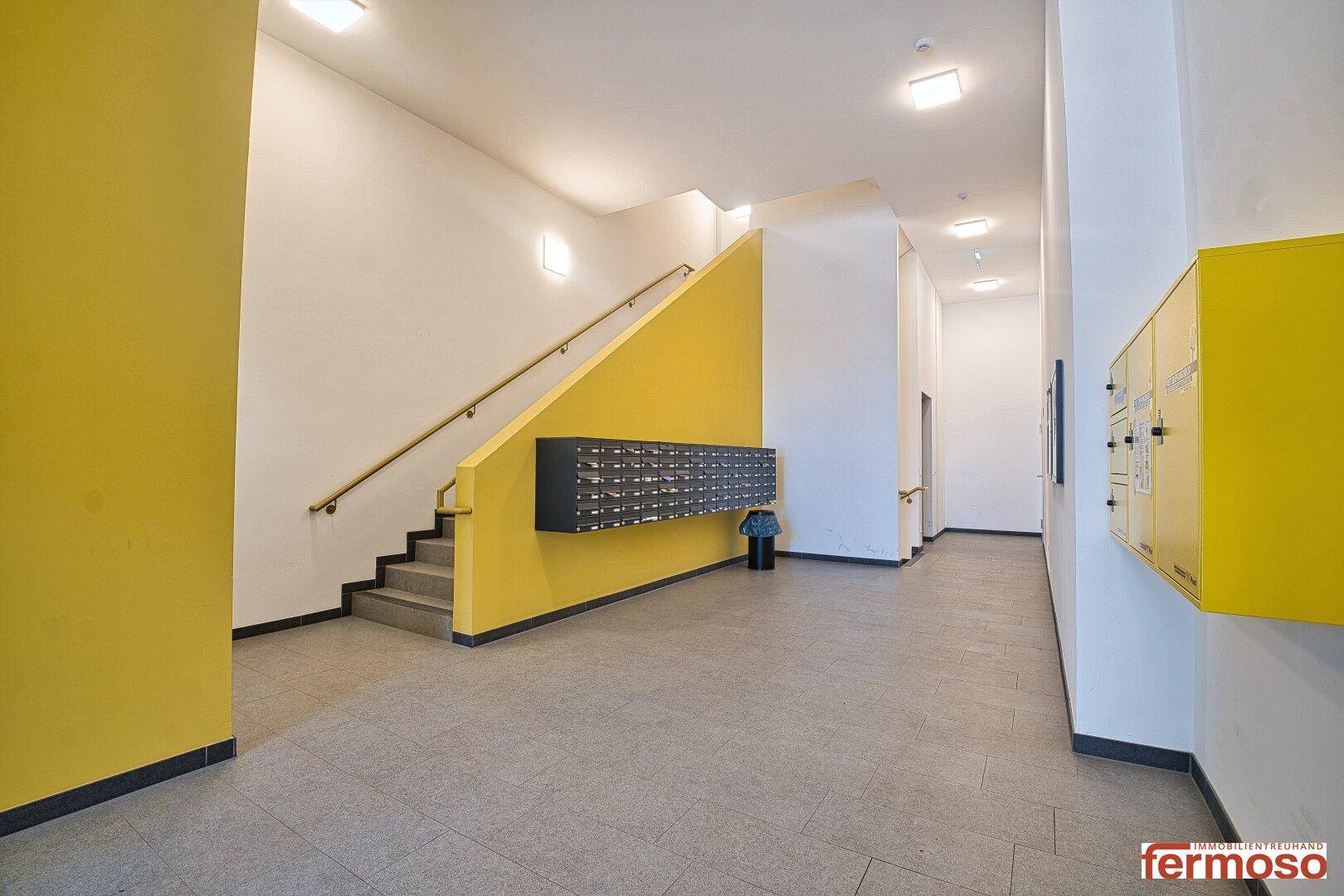 Moderner Eingangsbereich mit Treppe, Briefkästen und gelben Akzentwänden im Gebäude.