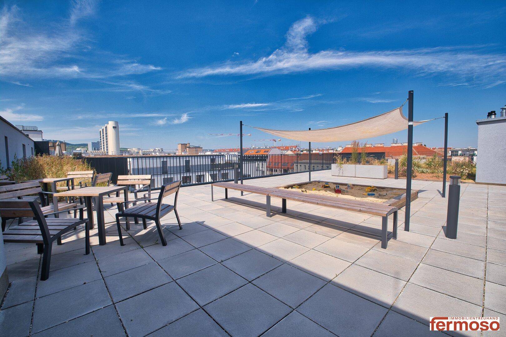 Große Dachterrasse mit Sitzgelegenheiten, Sonnensegel und Blick über die Stadt.