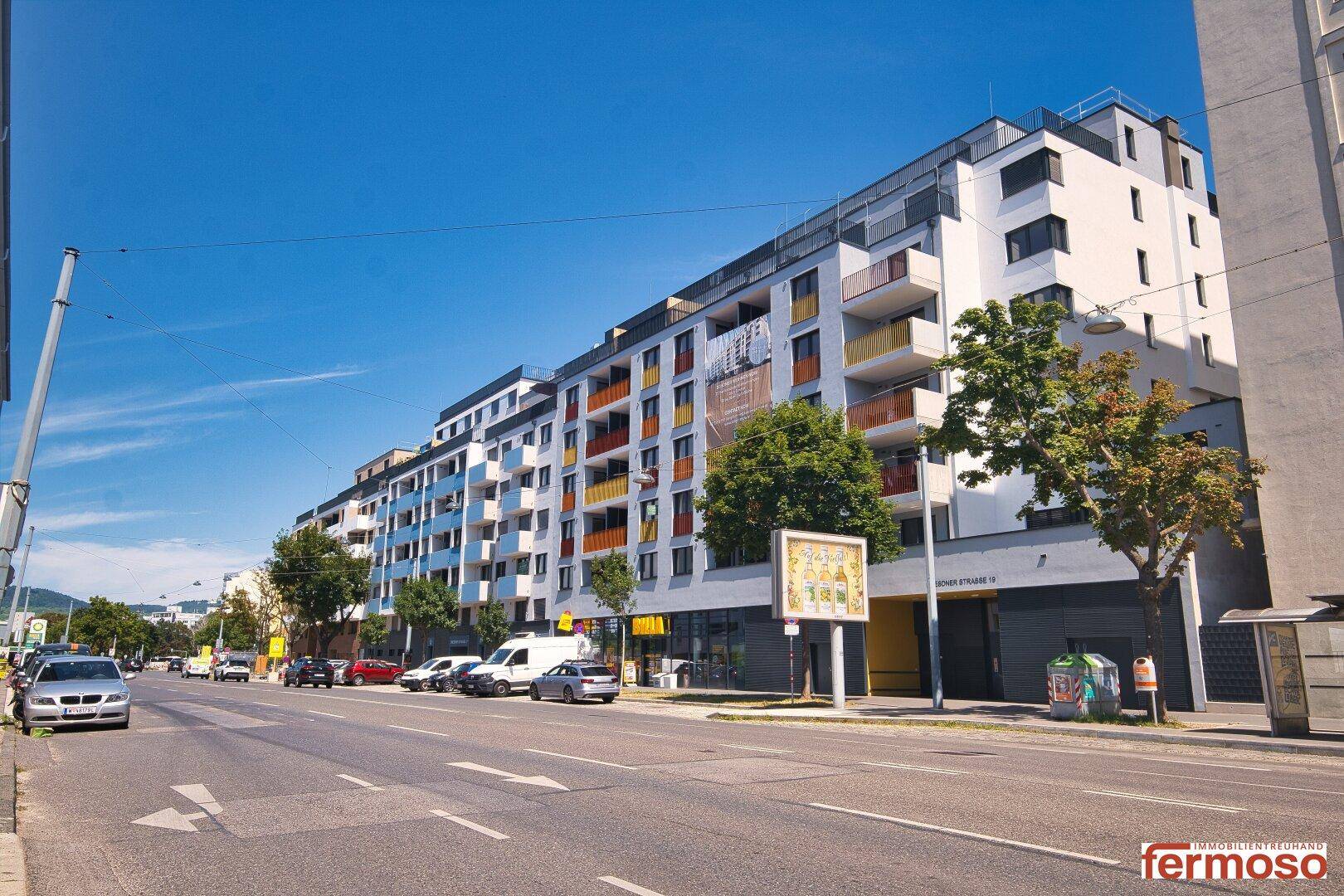 Moderne Wohngebäude entlang einer Straße mit farbigen Balkonen und Geschäften im Erdgeschoss.