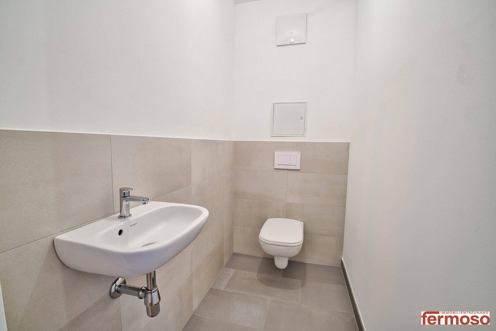 Modernes Gäste-WC mit wandhängender Toilette, kleinem Waschbecken und hellen Fliesen.