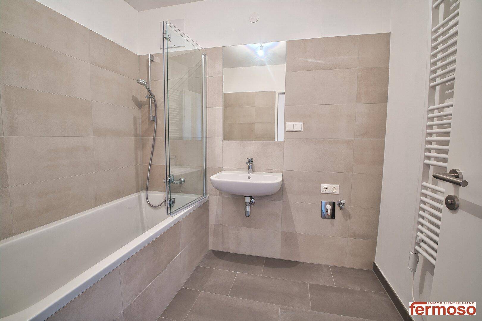 Modernes Badezimmer mit Badewanne, Duschabtrennung, Waschbecken und beheiztem Handtuchhalter.