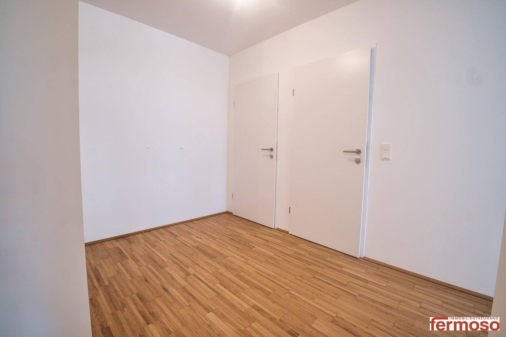 Leerer Raum mit Parkettboden und zwei weißen Türen, bietet Potenzial für verschiedene Nutzungen.