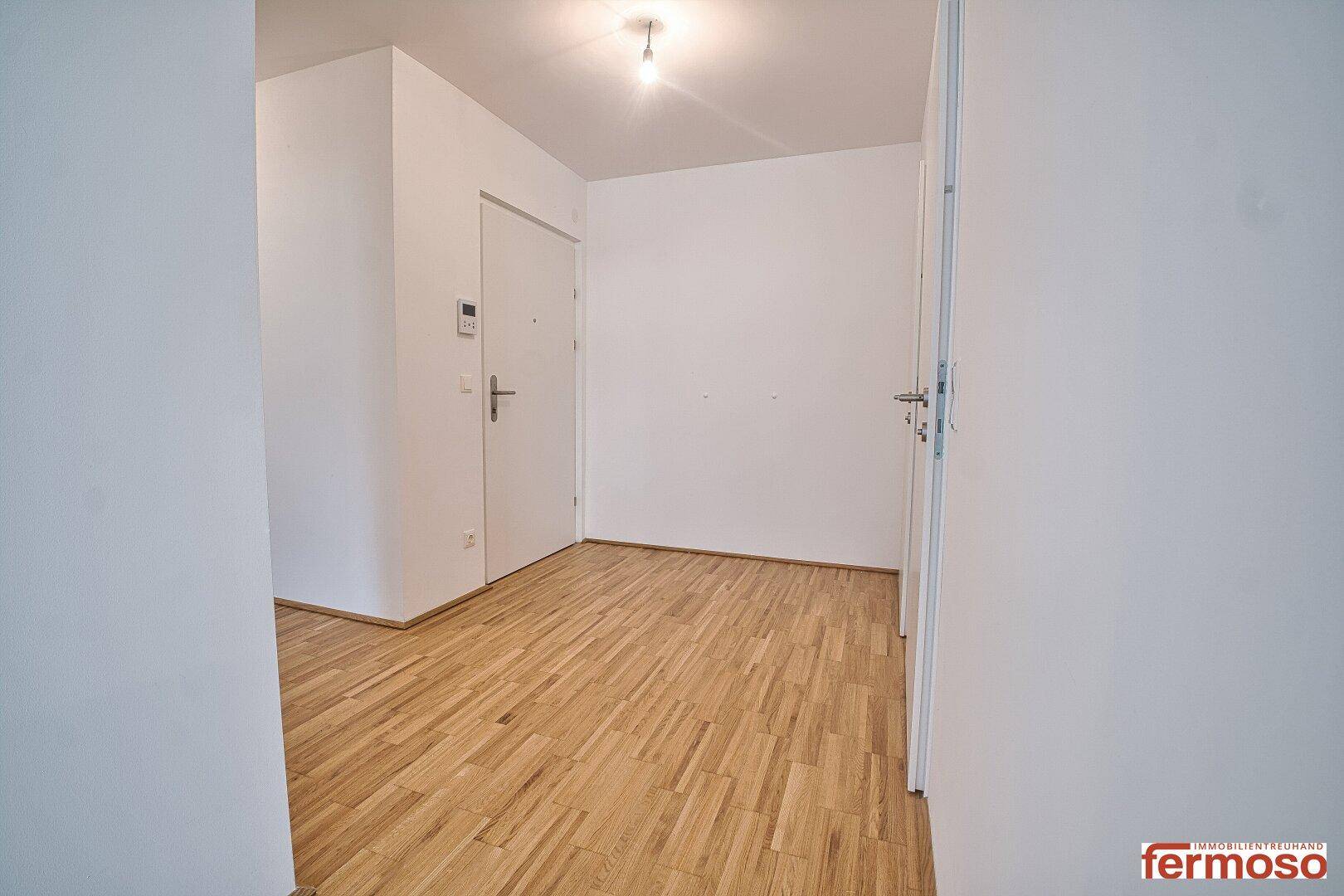 Heller Eingangsbereich mit Parkettboden und weißen Türen, führt zu weiteren Räumen der Wohnung.