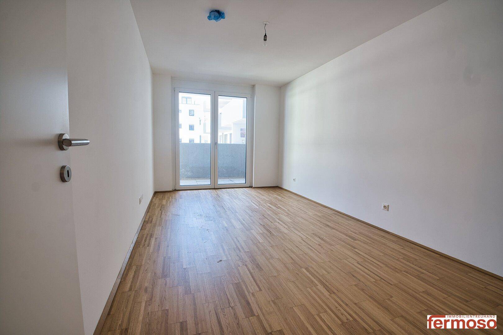 Heller, leerer Raum mit Parkettboden und Zugang zu einem Balkon, ideal als Wohn- oder Schlafzimmer.
