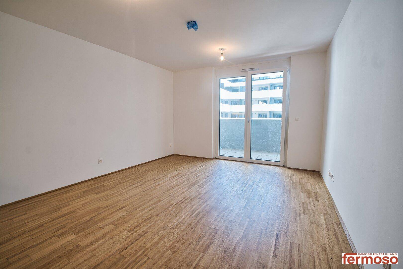 Geräumiger, heller Raum mit Parkettboden und Zugang zu einem Balkon, ideal für Wohnzwecke.