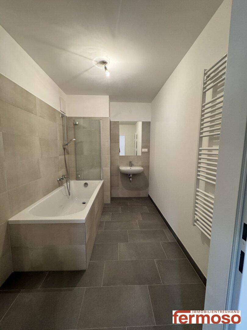 Modernes Badezimmer mit Badewanne, Dusche, Waschbecken und beheiztem Handtuchhalter.