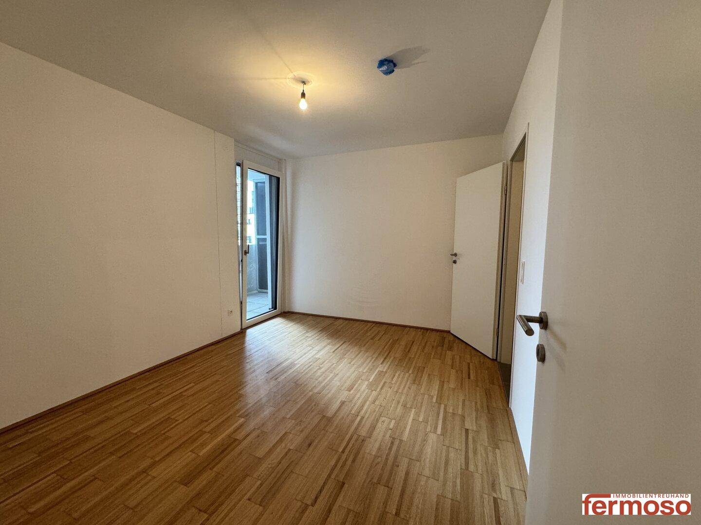 Helles Schlafzimmer mit Parkettboden und Zugang zu einem Balkon oder einer Loggia.