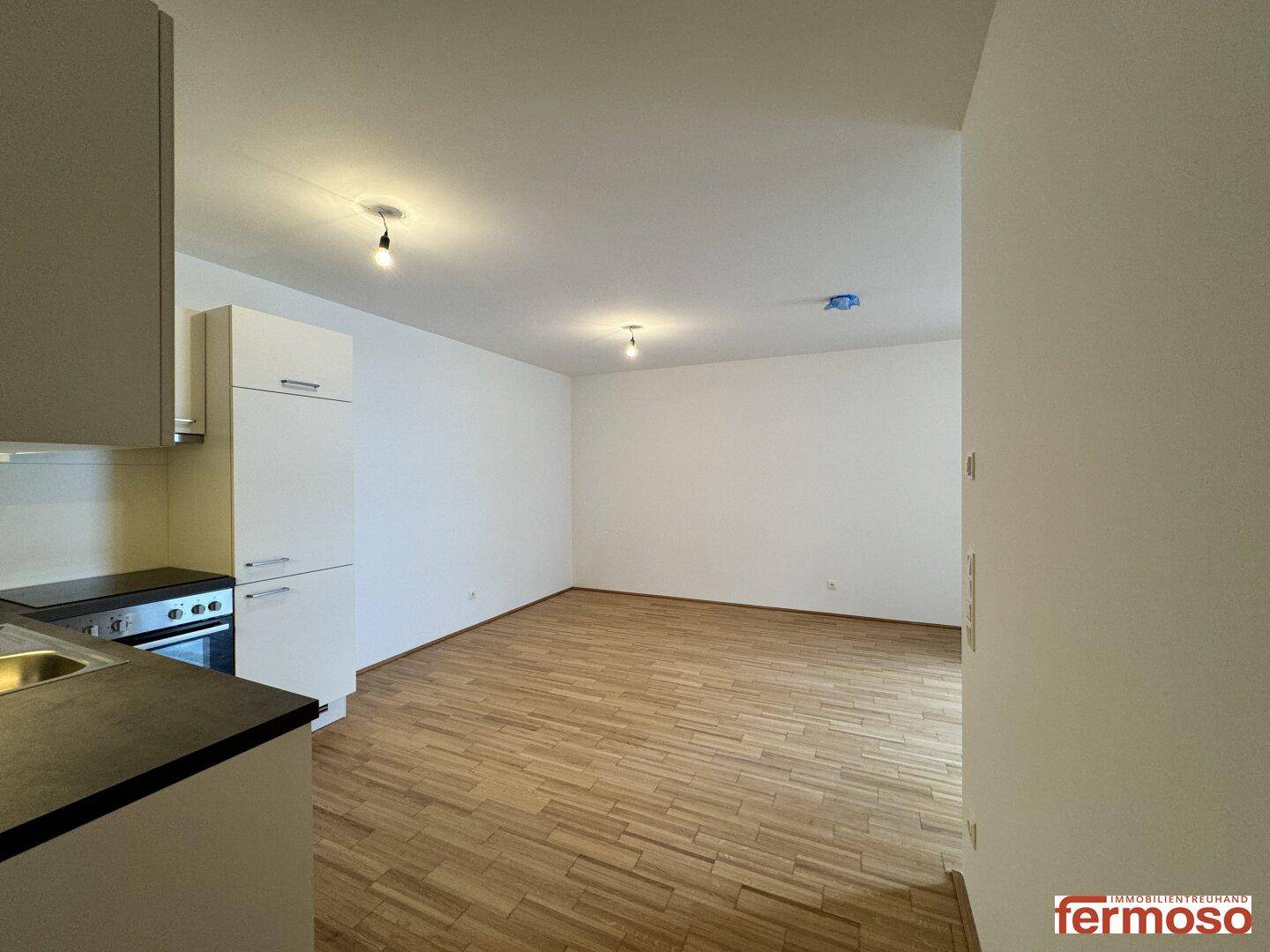 Offener Wohnbereich mit Parkettboden und Blick auf die moderne Küchenzeile im Hintergrund.