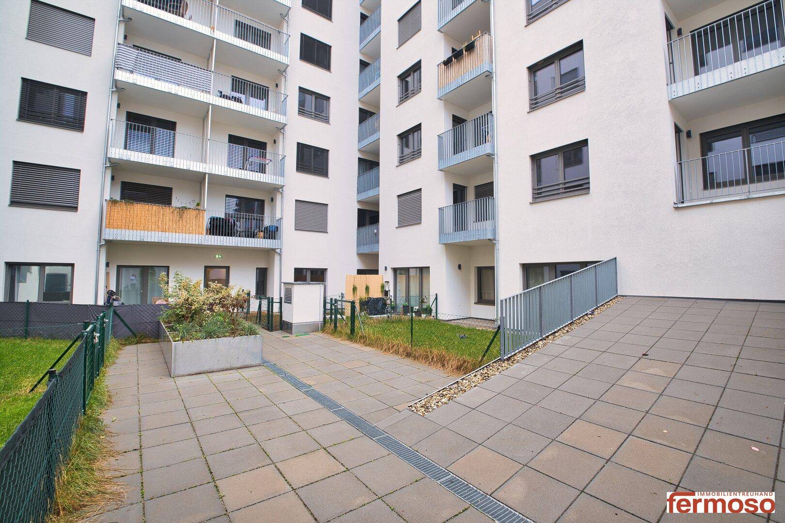 Gemeinschaftsgarten mit gepflasterten Wegen und Grünflächen zwischen den Gebäuden.