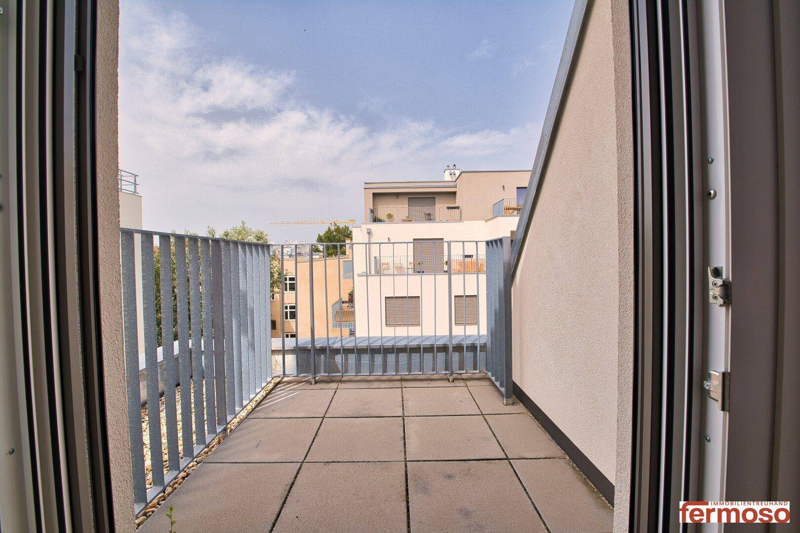 Heller Balkon mit Fliesenboden und Blick auf die Nachbarschaft.