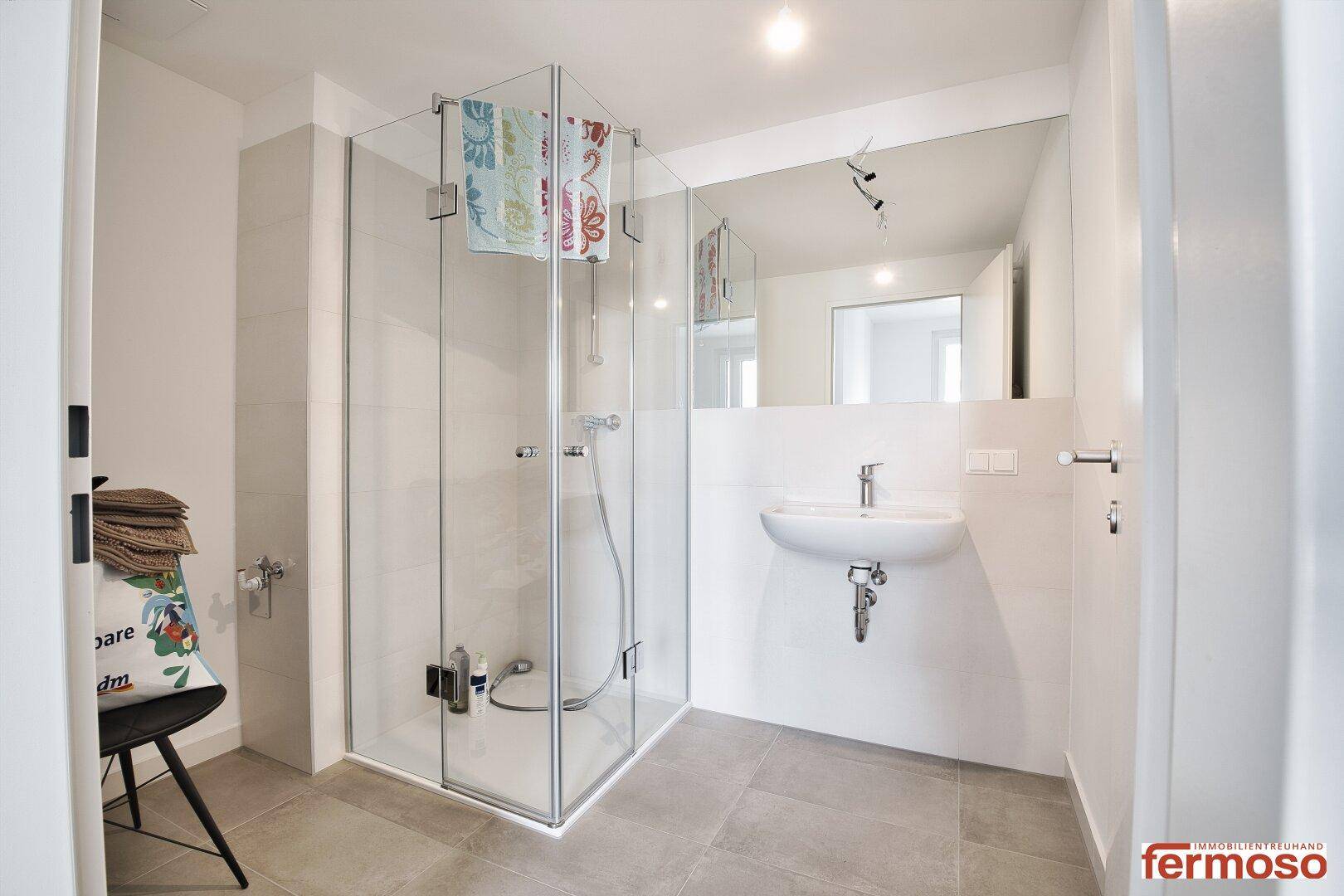 Modernes Badezimmer mit ebenerdiger Dusche, großem Spiegel und Einzelwaschbecken.