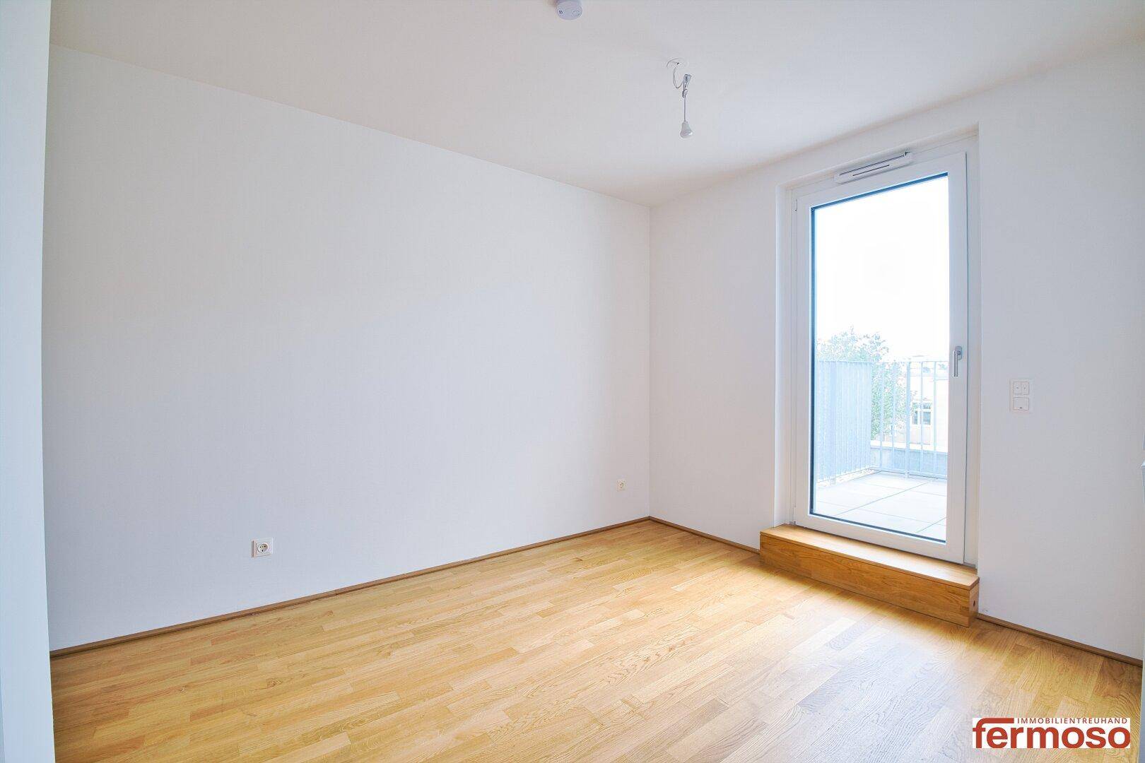 Helles Zimmer mit Parkettboden und Zugang zu einem kleinen Balkon.