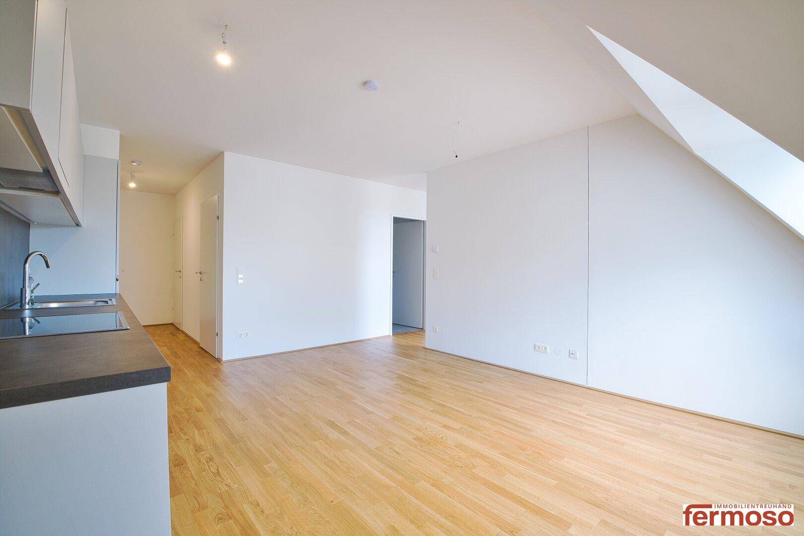 Geräumiger Wohnbereich mit integrierter Küchenzeile und Dachschrägenfenster.