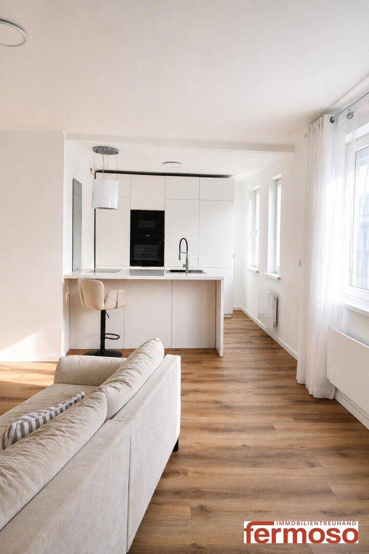 Moderne weiße Küche mit Kochinsel und Barhockern, offen zum Wohnbereich.