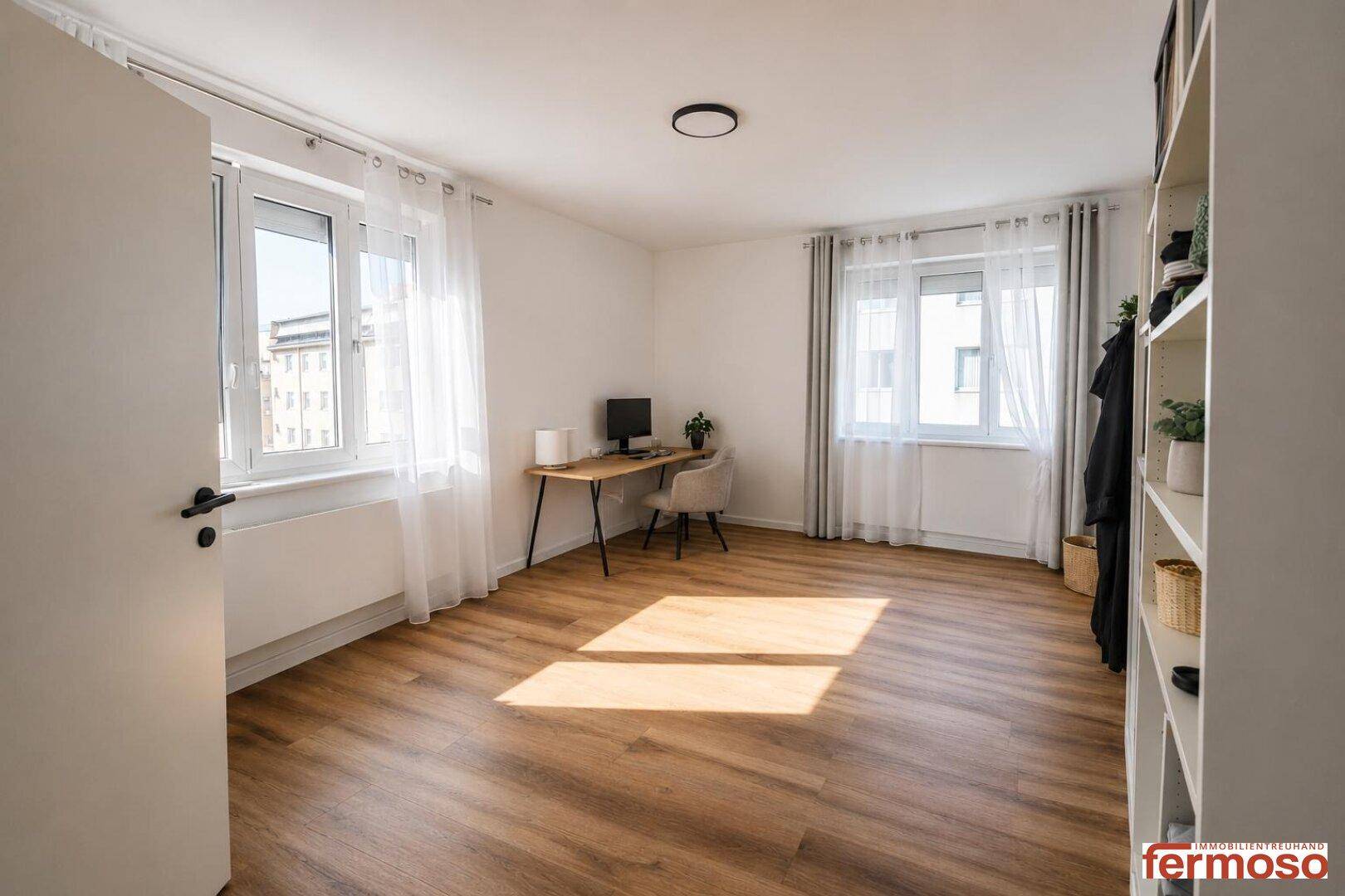 Helles Arbeitszimmer mit Holzboden, zwei Fenstern und einem Schreibtisch.