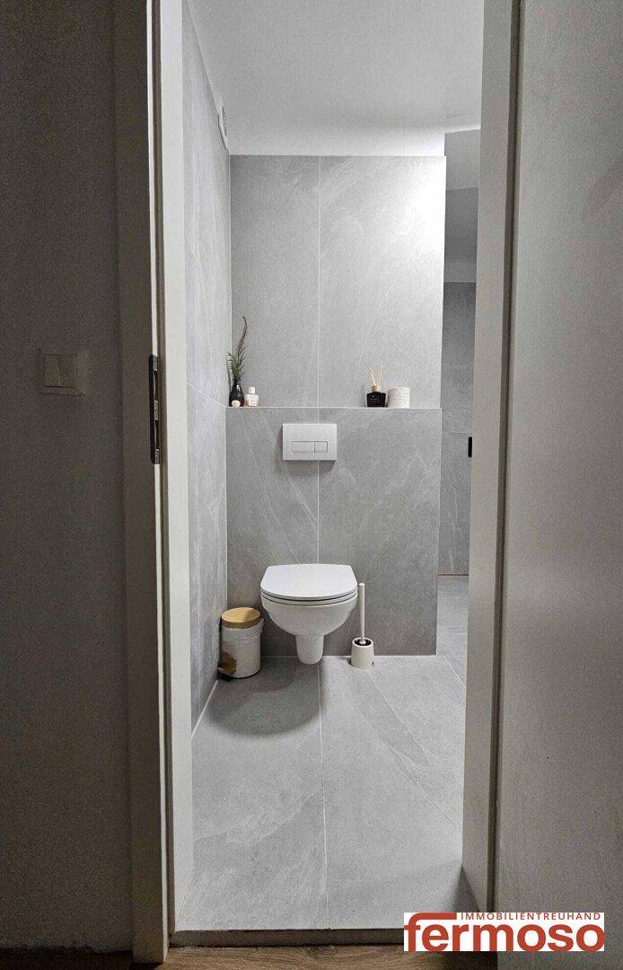 Modernes Gäste-WC mit grauen Fliesen und wandhängendem WC.