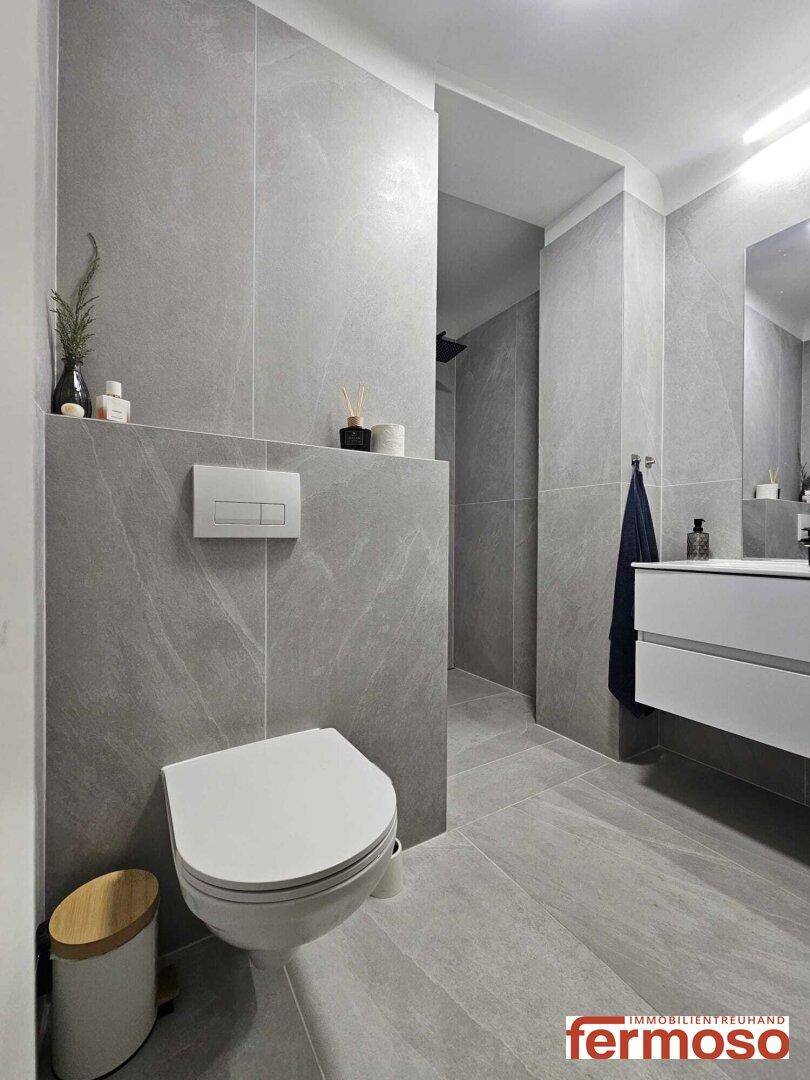 Elegantes Badezimmer mit grauen Fliesen, wandhängendem WC und modernem Waschtisch.