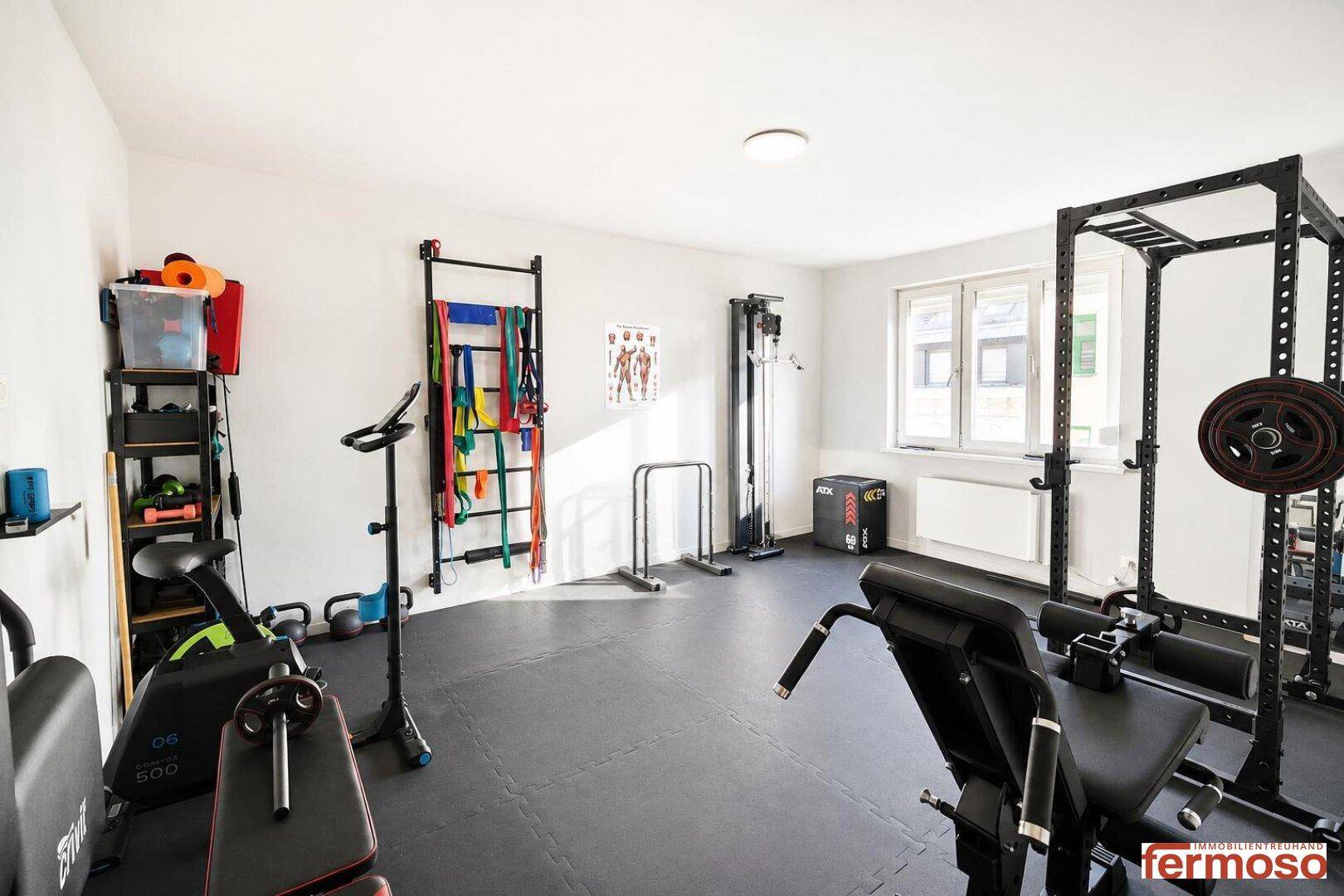 Geräumiger Fitnessraum mit Sportgeräten und Gummiboden für das Heimtraining.