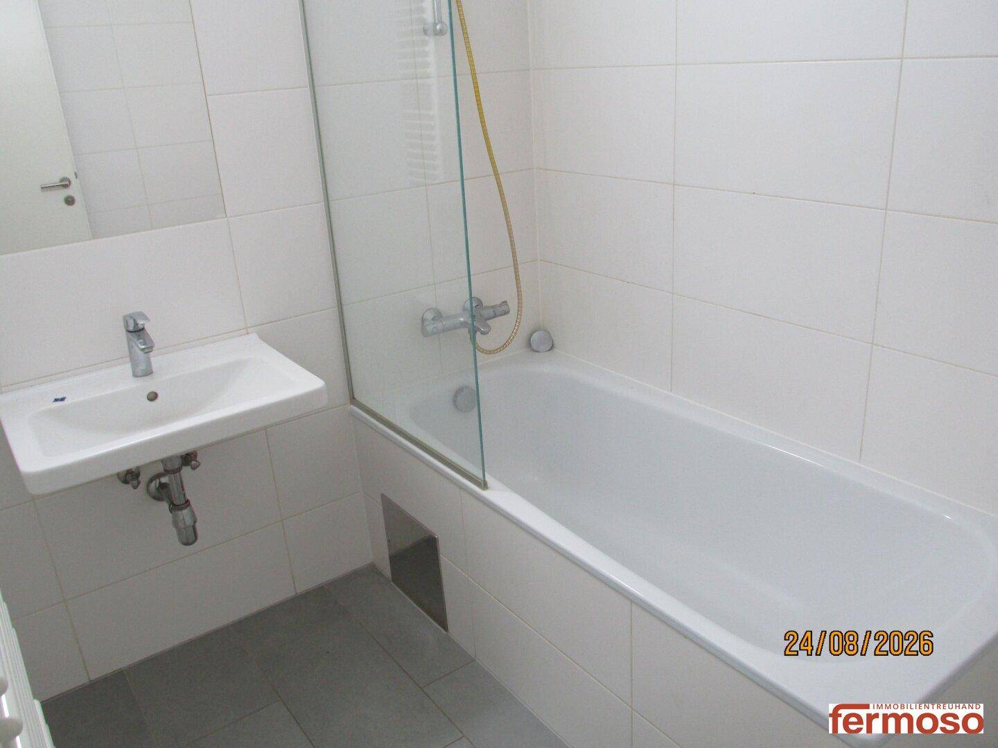 Helles Badezimmer mit Badewanne, Duschabtrennung und Einzelwaschbecken, modern gefliest.