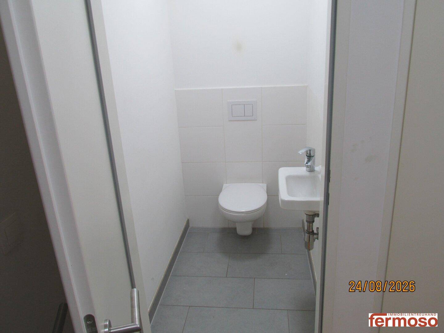 Kleines Gäste-WC mit Wand-WC und Handwaschbecken, modern gefliest und hell.